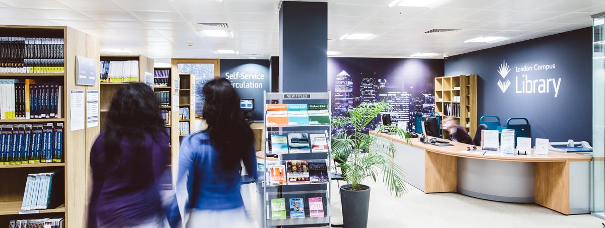 A view of London Library showing bookshelves, two students and the front desk